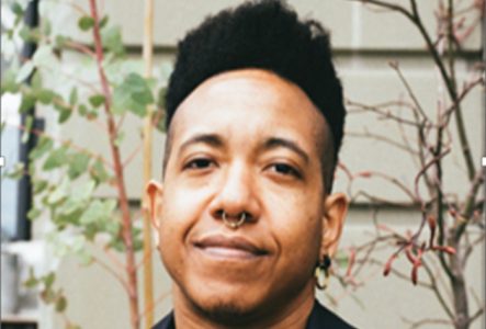 Une personne souriant face à l’objectif vêtu d’une chemise noire