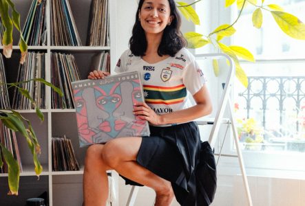 Une femme adulte souriante assise et tenant une pochette vinyle coloré tout en regardant la caméra