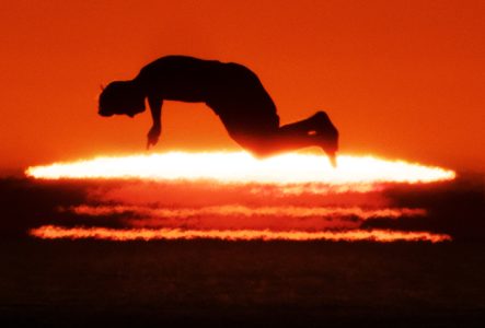 Photo contemporaine d’un coucher de soleil avec la silhouette d’un homme sautant parallèlement au soleil dans la pénombre.