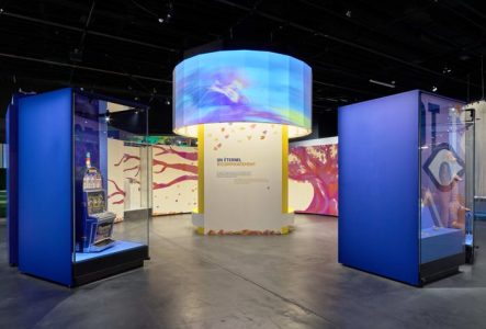 Prise de vue de l'exposition Le futur c'est quoi, on y voit au centre une projection en forme de rond sur une structure droite et sur les côtés des vitrines avec des objets.