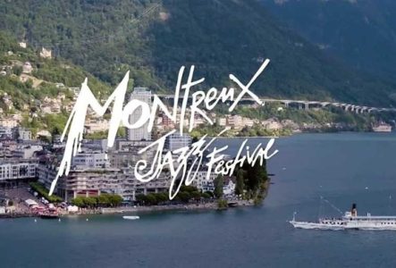 L'image montre une vue aérienne en plongée de la ville de Montreux, un grand bateau à vapeur traditionnel blanc.