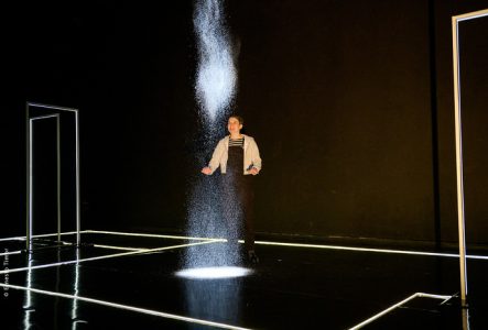 © Une jeune femme regarde tomber de la neige dans faisceau de lumière dans un espace créé avec des néons