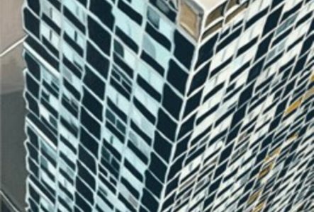 L'image est une vue aérienne d'un grand bâtiment avec une architecture moderne distinctive, mettant en évidence sa structure en grille de fenêtres. Les fenêtres sont disposées dans un motif, certaines réfléchissant la lumière, tandis que d'autres sont plus sombres ou probablement cachées par des ombres. En bas de l'image, on peut voir les lettres "nsnz" en texte blanc et gras. Le bâtiment a une façade en verre, et l'ensemble de l'image présente un contraste dynamique entre la lumière et l'ombre…