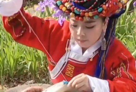 Jeune fille Moso qui coud un vêtement à la main.