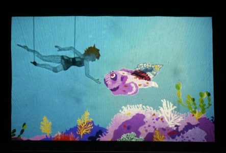 La figurine d'une fille en marionnette à tiges suit un coquillage au fond de l'océan au dessus d'un banc de corail coloré.