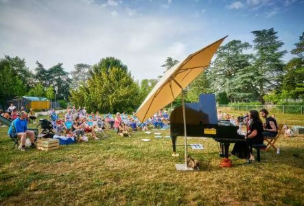 Pianoségarés Un piano à queue et du public aui écoute assis dans l'herbe