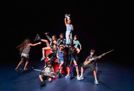Un groupe d'enfants et adolescents sont sur scène et forme un ensemble joyeux et décalé.