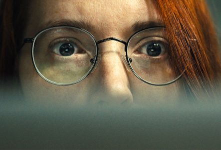 © FIFDH2025_Hacking Hate Gros plan sur le visage d'une personne aux cheveux roux et aux lunettes rondes, fixant intensément un écran.