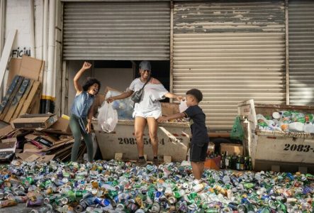Une mère et ses enfants sautent en souriant dans un tas de déchets (des canettes vides)
