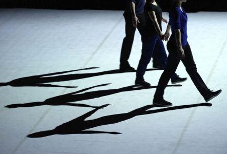 Trois danseurs marchent en ligne, avec un focus sur leurs ombres.