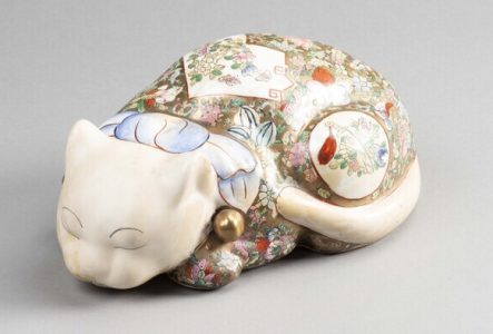 Figurine de chat en porcelaine qui provient de Chine et qui est daté du 20e siècle. Il est allongé, les yeux fermés. Sur son dos se trouve de jolis décors de fleurs.