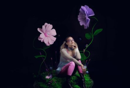 Portrait de Louisadonna, assise sur de l’herbe et entourée de grandes fleurs colorées, modélisées en 3D.