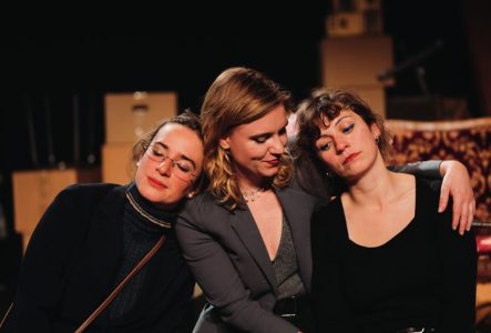 Trois jeunes femmes assises sur un canapé . Devant elles, un carton de déménagement avec trois jolies tasses à thé dessus