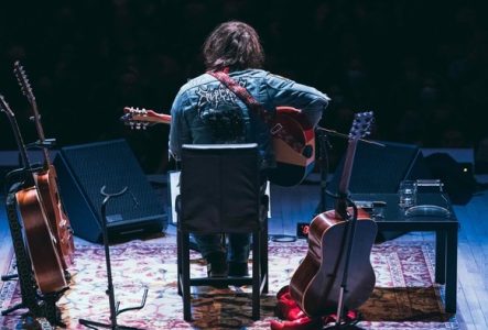 Photo de dos de Ryan Adams sur scène avec plusieurs guitares acoustiques autour de lui