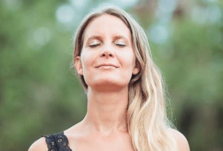 Circé Luginbühl, sophrologue et organisatrice de l'évènement, est vue de face, dans une posture méditative et les yeux fermés. Derrière elle, on discerne un fond flouté d'arbres.