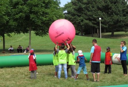 Un groupe d'enfant en train de jouer avec un ballon rose gigantesque, tenu au-dessus de leurs têtes.