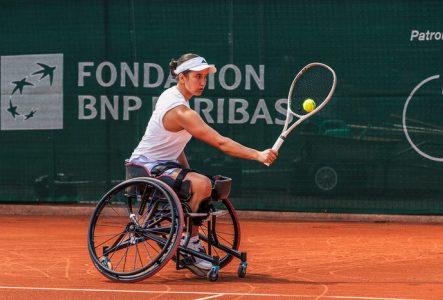 On voit sur cette image, une joueuse de tennis en fauteuil roulant en pleine action sur un court en terre battue.
