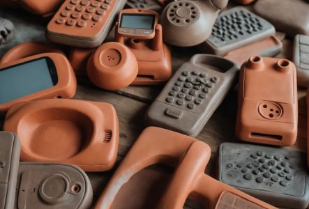 Sur une table en bois sont posées des sculptures en terre d'appareils électroniques, dont des smartphones