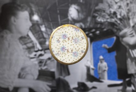 Un bouton en céramique au fond blanc avec des décors floraux et à la bordure dorée est disposé sur une image en noir et blanc et légèrement floue représentant des femmes.