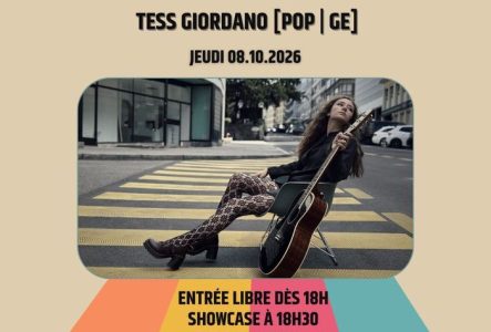 L'artiste est assise sur une chaise,  la tête penchée vers l'arrière et elle tient la guitare avec une main.