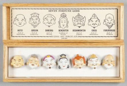 Une boîte en bois dans laquelle se trouve des boutons représentant les visages de dieux japonais.