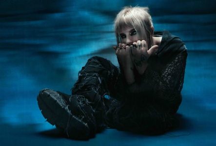 Photo de l'artiste assise par terre recroquevillée sur elle même avec les mains sur sa bouche
