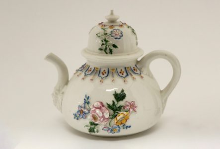 Théière en porcelaine sur laquelle sont peintes en relief des fleurs.