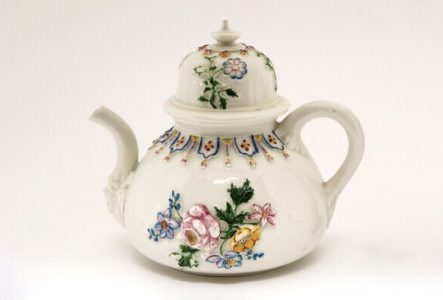 Théière en porcelaine sur laquelle sont peintes en relief des fleurs.