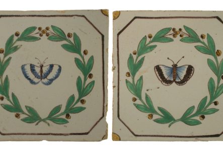 Deux carreaux en faïence sur lesquels un papillon et une couronne de houx sont peints.