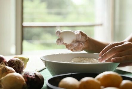 Plan serré sur des mains en train de casser un œuf dans un bol rempli de farines