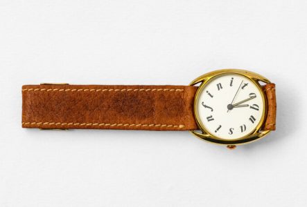 Montre bracelet au cadran doré et bracelet en cuir, avec le mot "quasinfito" en lettres italiques remplaçant les chiffres tout autour du cadran.