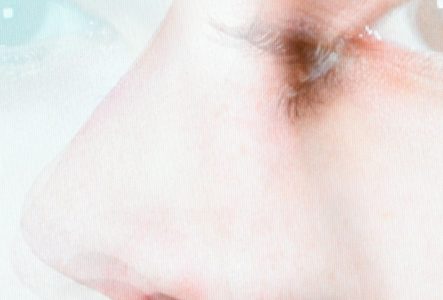 Portrait d'une jeune femme en t-shirt rose dont le visage est presque dissimulé par les branches d'un arbre.