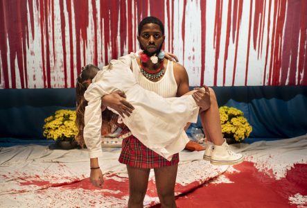 Sur cette image, il y a un homme debout portant dans ces bras une femme vêtu d'une robe blanche.